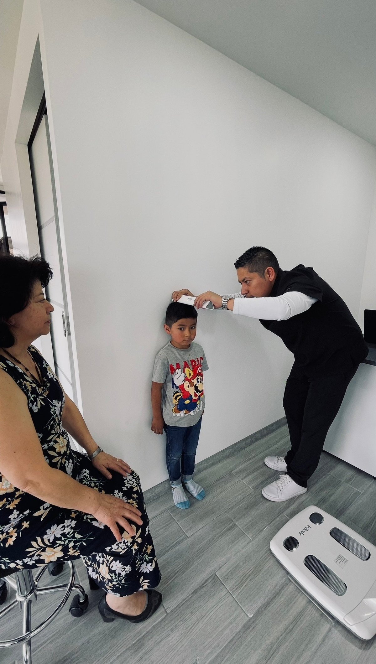 Healthcare professional measuring height of young child while woman watches during medical appointment