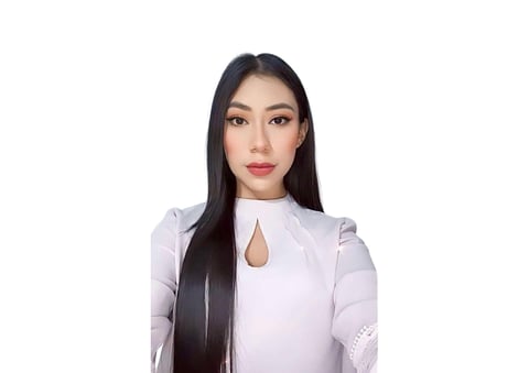 Woman with long black hair wearing a light pink long-sleeved top with a keyhole neckline, looking at camera against white background