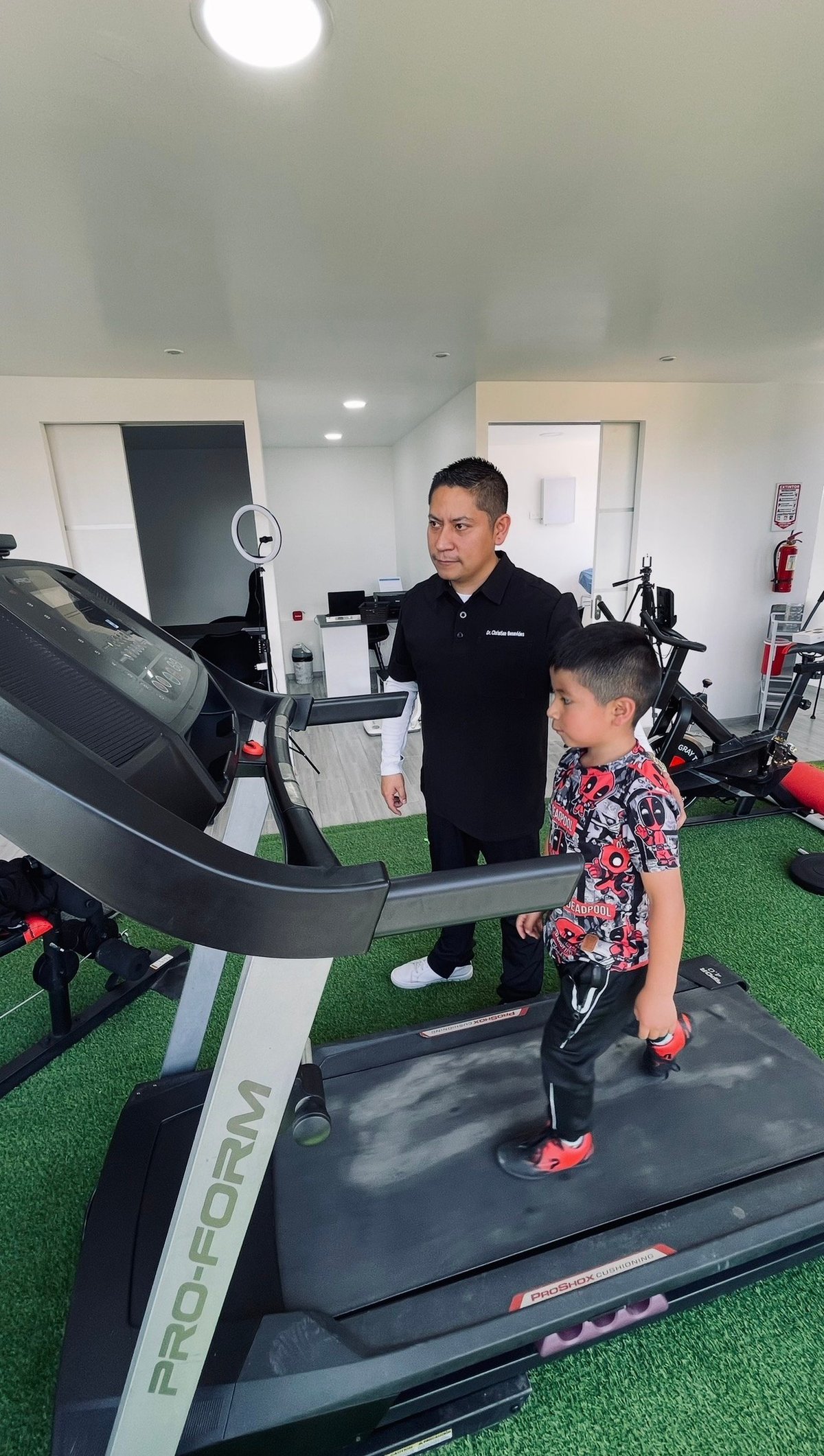 Adult trainer instructing young child on ProForm treadmill in modern gym facility with green flooring