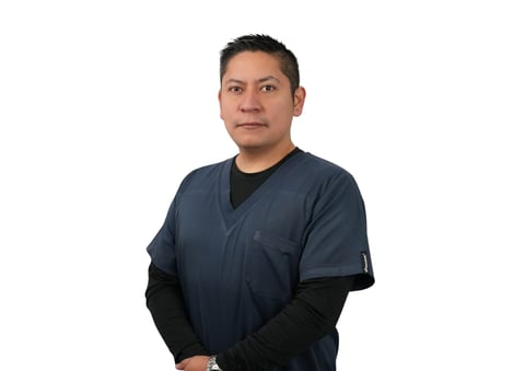 Professional headshot of a man wearing a dark blue medical scrub top and black long-sleeved undershirt against a white background